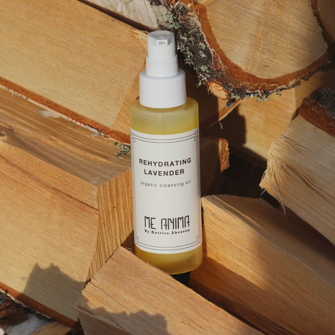 Me Anima Cleansing Oil Rehydrating Lavender placerad mot staplad ved i soligt ljus, ekologisk rengöringsolja med lavendel.