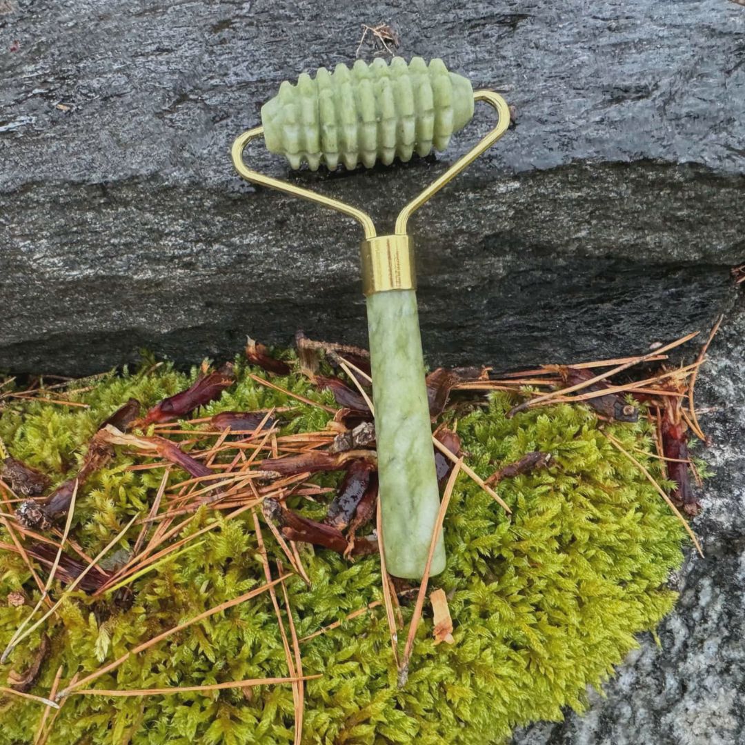 Grön jade gua sha roller från Me Anima ligger på mossa och sten i naturen