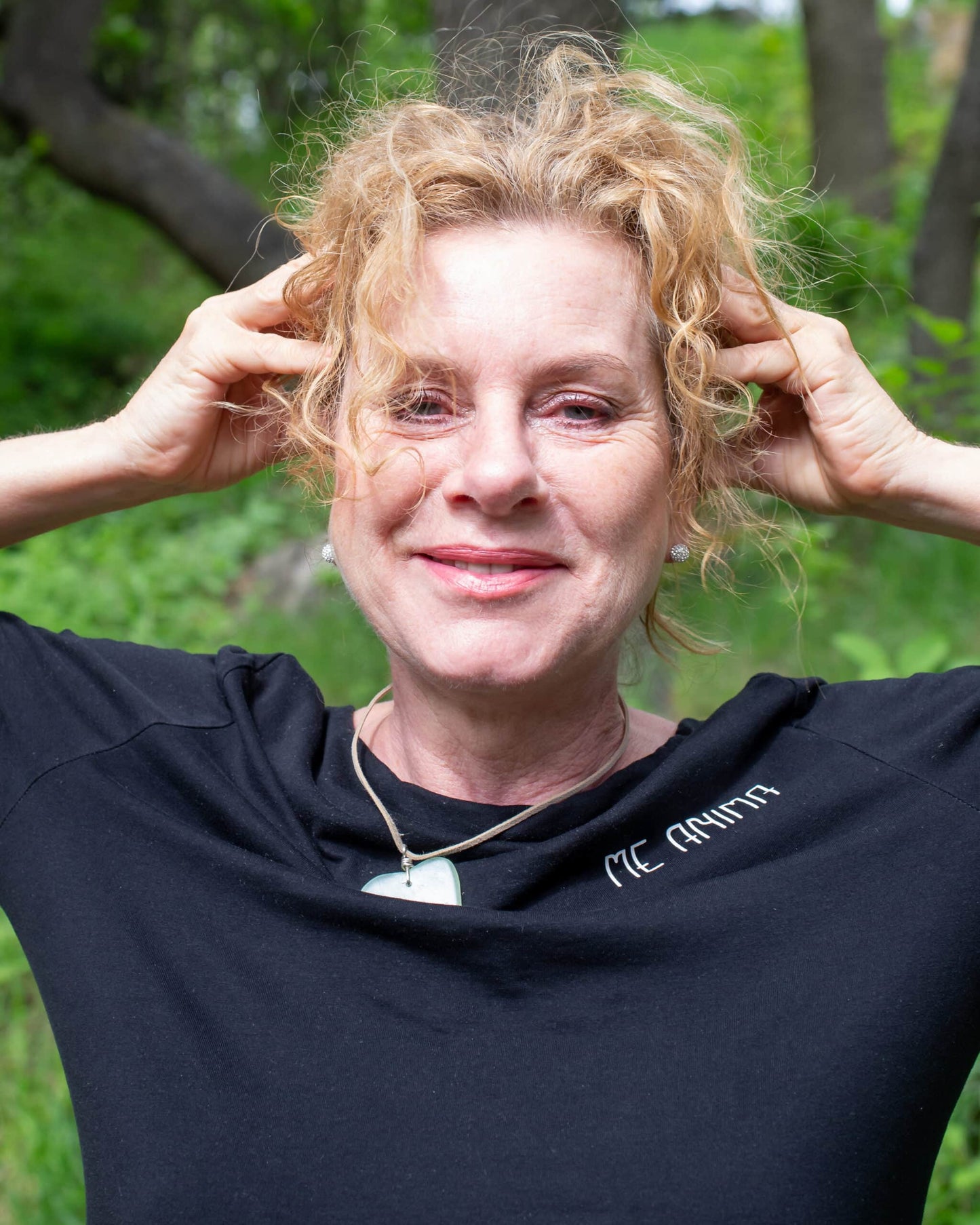 Katties Åkesson, grundare av Me Anima, ler i grönskan och visar ansiktsgympaövning.