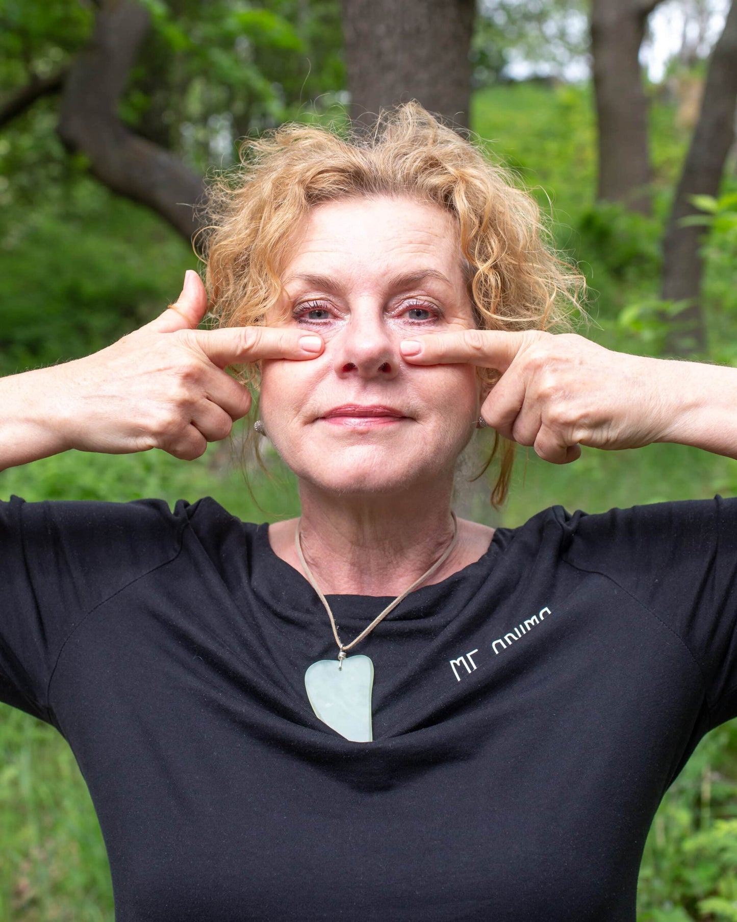 Katties Åkesson grundare av Me Anima visar ansiktsgympaövning för området under ögonen i naturmiljö