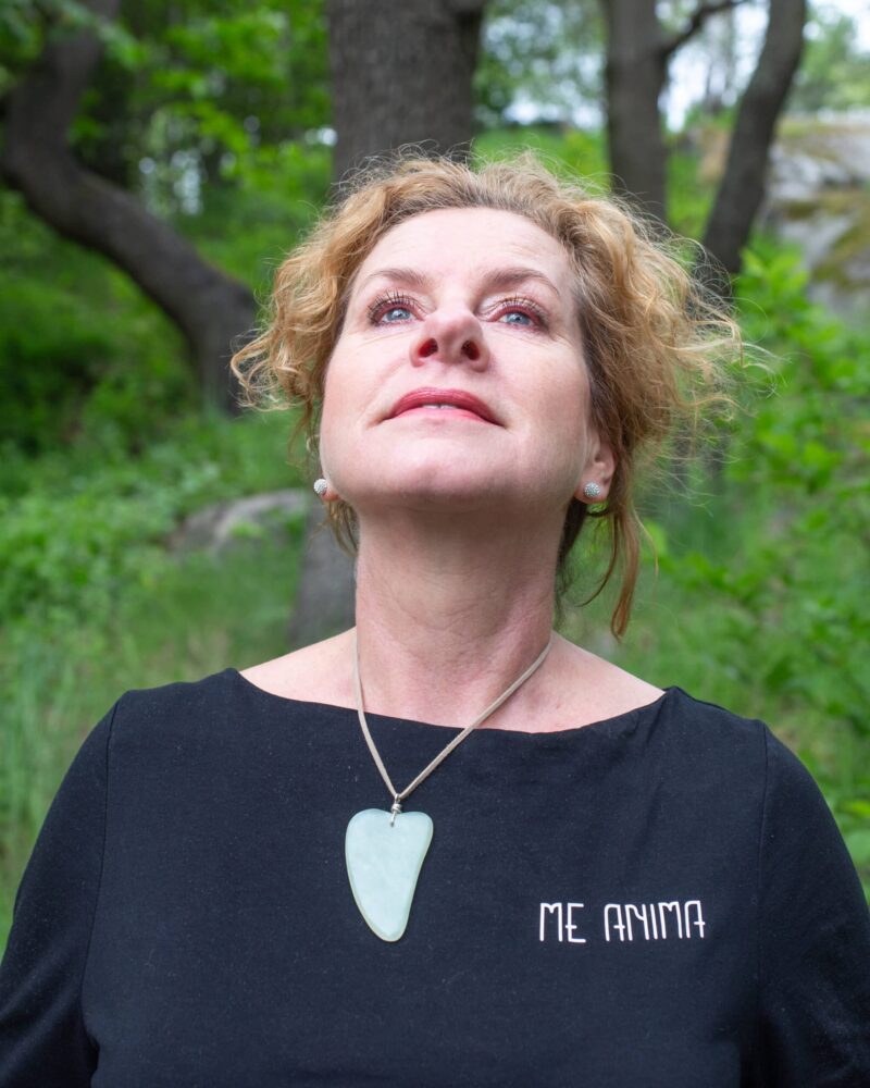 Kvinna bär Gua Sha-verktyg från Me Anima som halsband under ansiktsgympa – en naturlig metod för att stärka ansiktsmuskler, öka blodcirkulationen och främja lyster i huden.