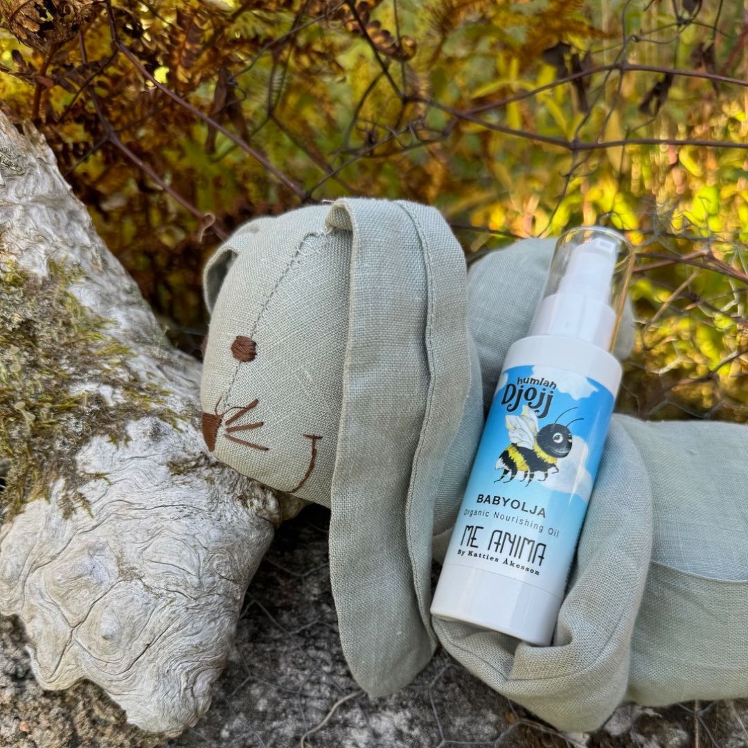 Me Anima babyolja Humlan Djojj placerad bredvid ett mjukt gosedjur i naturmiljö