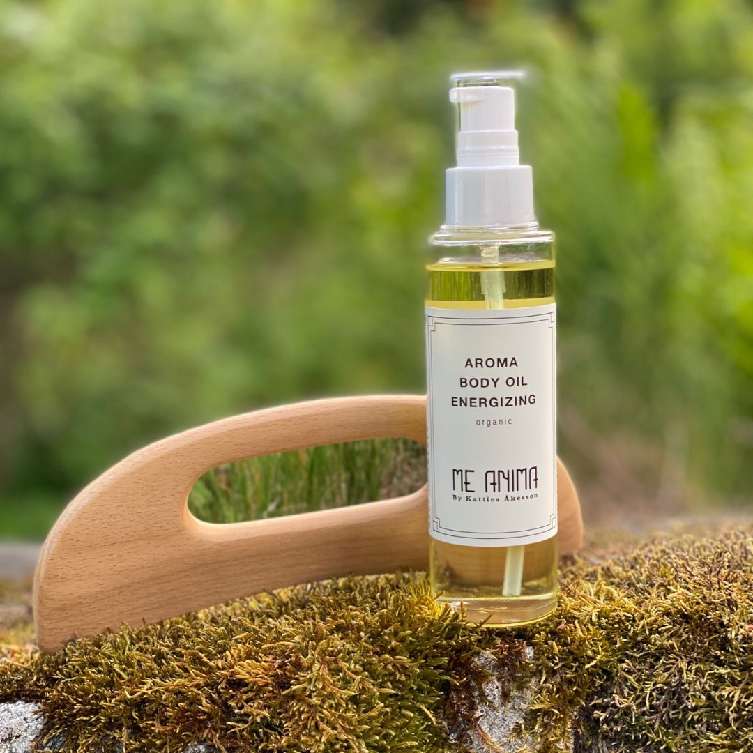 Me Anima kroppsolja Energizing placerad på mossa bredvid Gua Sha i trä i grön naturmiljö
