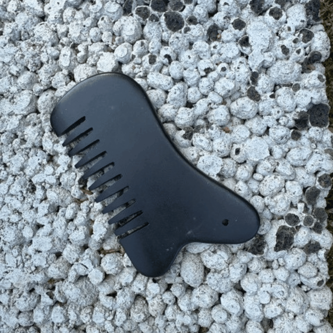 Me Anima Gua Sha Bian-sten i svart natursten för massage av hårbotten och kropp, placerad på ljus stenbakgrund.