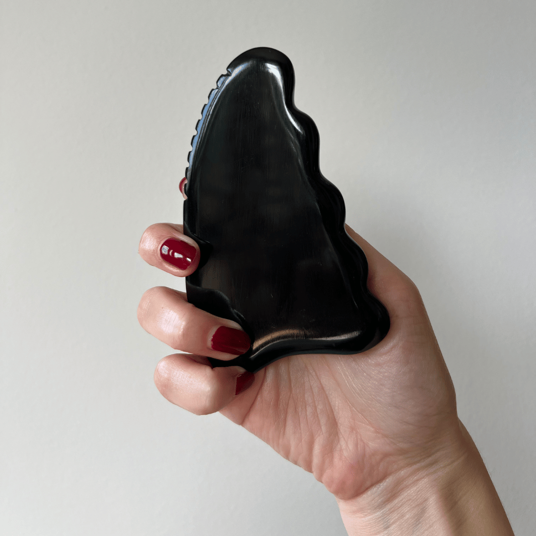 Hand som håller Me Anima Gua Sha Bian sten med vågig form, designad för att öka blodcirkulationen, stimulera lymfdränage och ge huden en värmande, energigivande känsla.