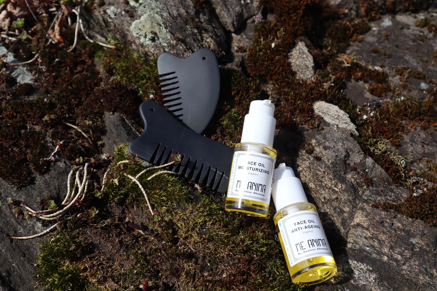 Me Animas Face Oil Anti-Ageing och Face Oil Moisturizing tillsammans med Gua Sha-verktyg placerade på sten och mossa – naturlig miljö för ansiktsmassage och egenvård.