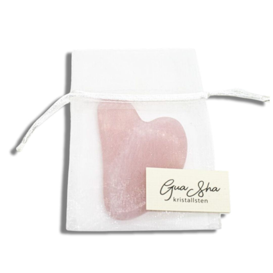 Gua Sha i rosenkvarts från Me Anima i vit organzapåse – ett hjärtformat verktyg för ansiktsmassage som stimulerar lymfsystemet, ökar blodcirkulationen och ger huden en naturlig glow.