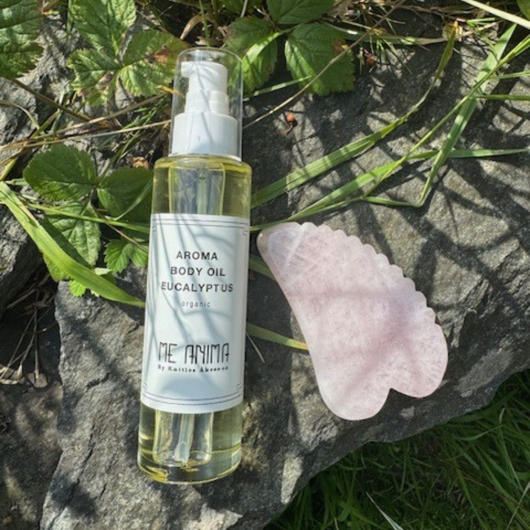 Me Anima kroppsolja Eukalyptus och Gua Sha-verktyg i rosenkvarts placerade på sten i naturmiljö