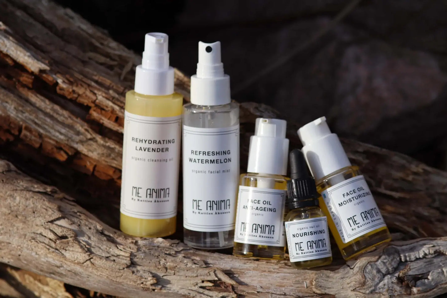 Me Anima hudvårdsprodukter – Rehydrating Lavender Cleansing Oil, Refreshing Watermelon Facial Mist, Face Oil Anti-Ageing, Face Oil Moisturizing och Nail Oil Nourishing – fotograferade på naturligt trä i solljus.