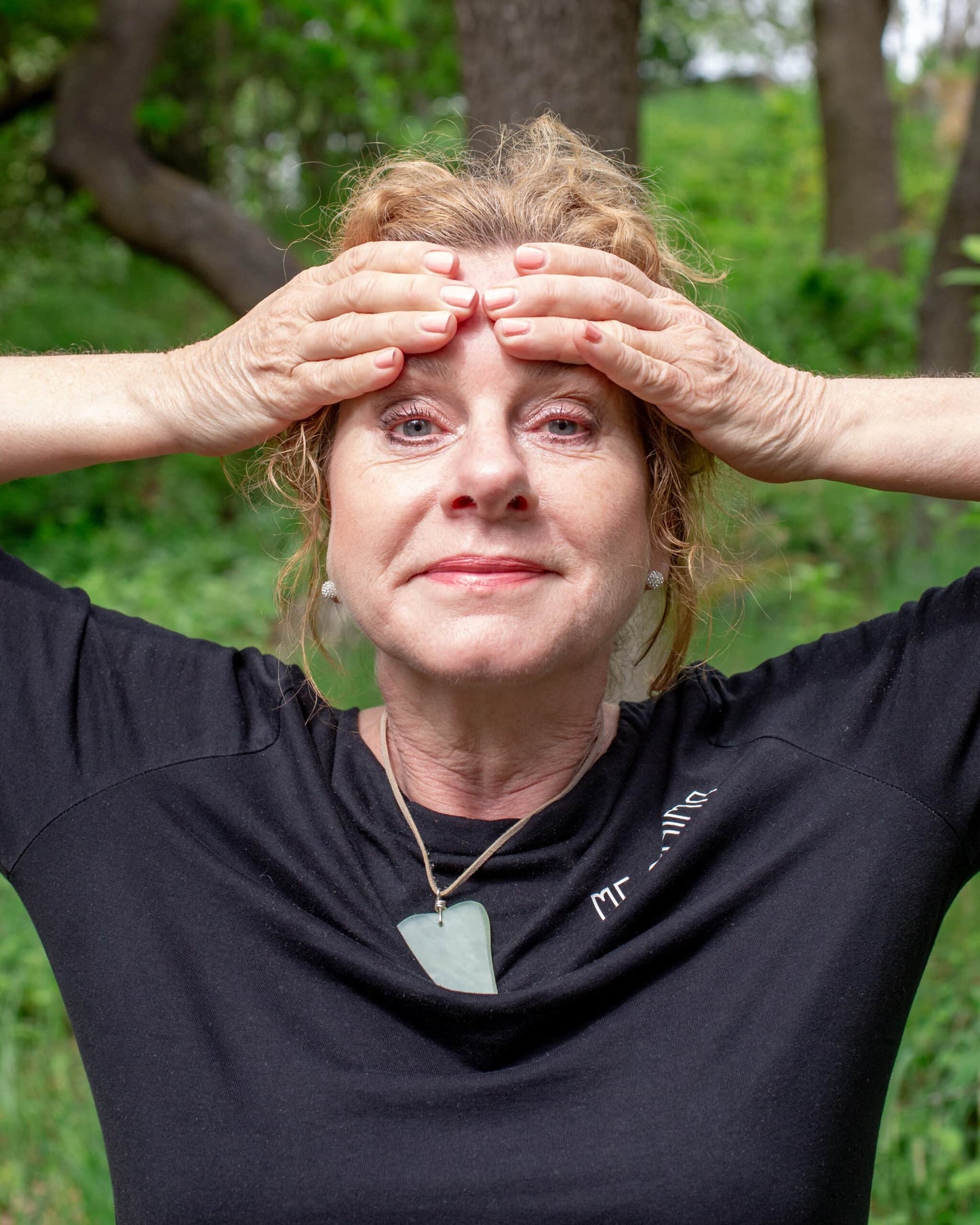 Katties Åkesson, grundare av Me Anima, visar ansiktsgympa med fokus på pannan för att släppa spänningar och främja cirkulation, iförd Gua Sha-hänge i grön sten.